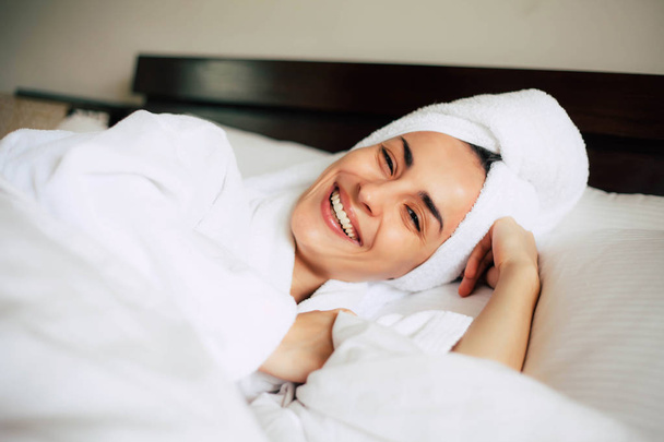Joke mood. Pretty girl after taking a shower in bath towel and bathrobe smiling sincerely right into the camera of her fiance. - Foto, afbeelding