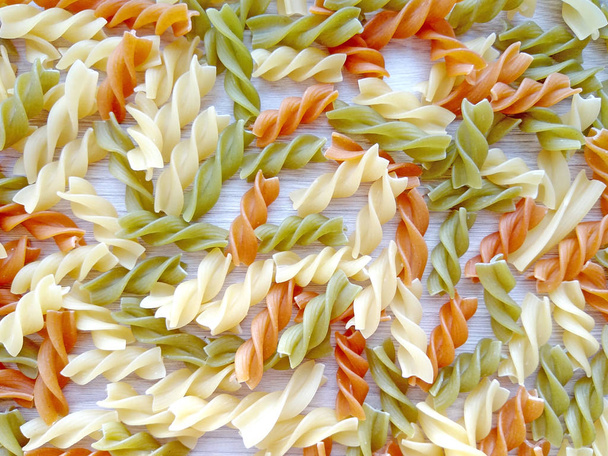 Sfondo di cibo italiano strutturato - pasta fusilli cruda colorata su tavola di legno. Vista dall'alto piatto lay close up fotografia
 - Foto, immagini