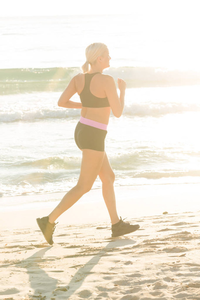 若いスポーツ女性がビーチでジョギングします。 - 写真・画像