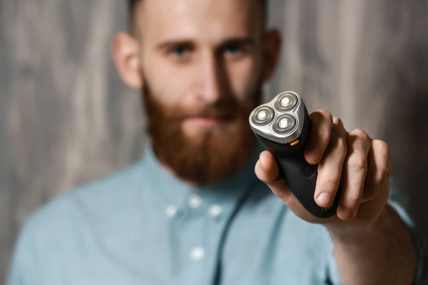 Hombre barbudo con afeitadora eléctrica sobre fondo gris
 - Foto, Imagen