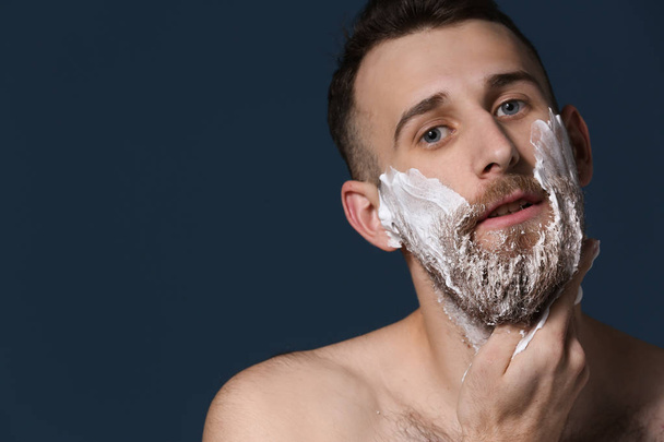 Uomo barbuto che applica schiuma da barba su sfondo scuro
 - Foto, immagini