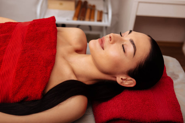 Peaceful dark-haired attractive woman lying on massage bed - Zdjęcie, obraz