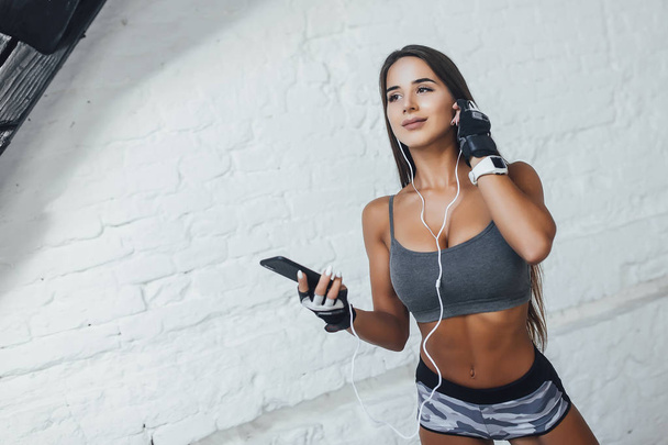 woman in sportswear with earphones listening music on smartphone at gym - Photo, image
