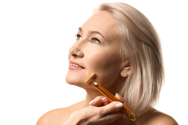 Mature woman with facial massage tool on white background - Photo, Image