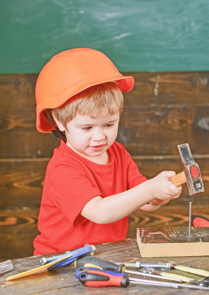 Safety at workplace. Little kid in orange helmet hammering nails. Cute boy playing with tools - Foto, imagen