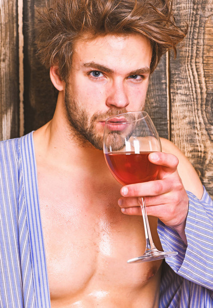 Пийте вино і розслабтеся. Хлопець привабливо розслабляється з алкогольним напоєм. Чоловік сексуально мокра шкіра грудей після ванни тримає келих. Бакалавр насолоджується вином після ванни. Махоїдне волосся зневоднює розкішне вино
 - Фото, зображення