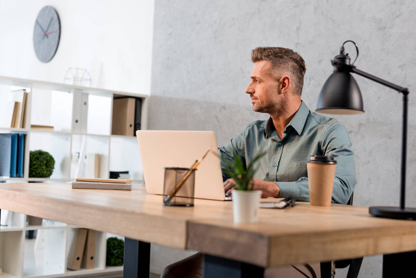 handsome businessman sitting near laptop in modern office - Фото, зображення