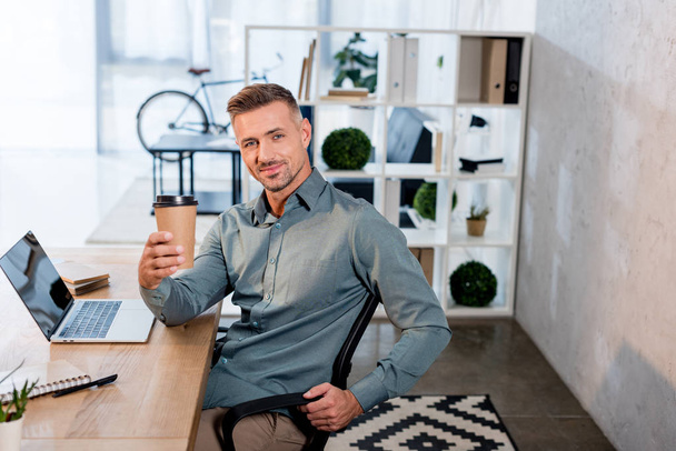 cheerful businessman holding paper cup in modern office - Fotó, kép