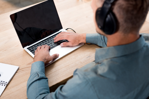 selective focus of man listening music in headphones while using laptop with blank screen - Photo, Image