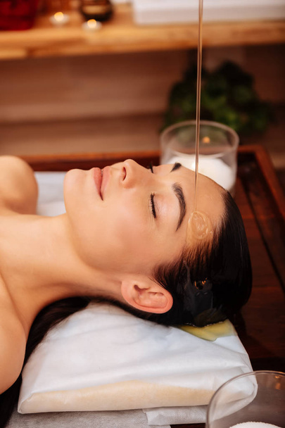 Dark-haired female client calmly lying on wooden table during treatment - Foto, Imagem