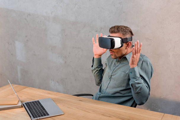 shocked businessman wearing virtual reality headset while sitting near laptop in office - 写真・画像