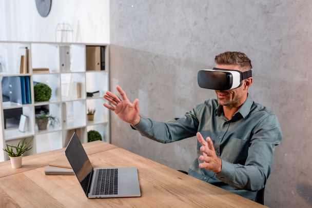 hombre de negocios con auriculares de realidad virtual mientras está sentado en la oficina cerca de la computadora portátil
 - Foto, Imagen