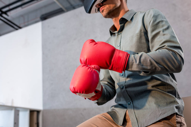 cropped view of businessman wearing virtual reality headset and boxing gloves in office - Photo, image