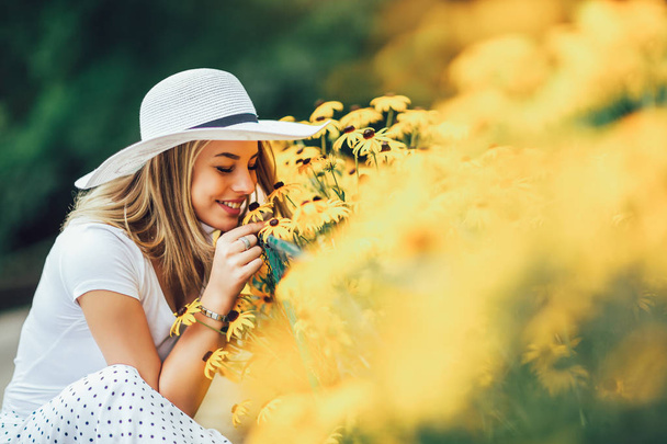 Mooie jonge vrouw ruiken gele bloem in het park. - Foto, afbeelding