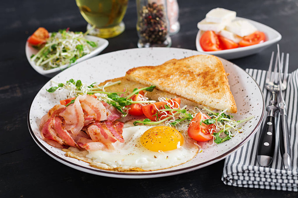Английский завтрак - тосты, яйца, бекон и помидоры и салат из микрозелени
. - Фото, изображение