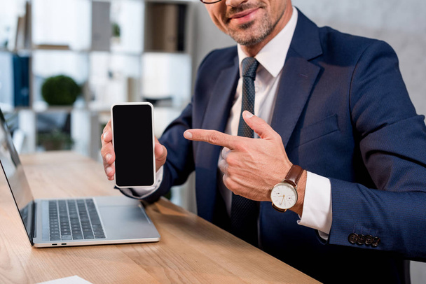 обрізаний вид веселого бізнесмена, який вказує пальцем на смартфон з порожнім екраном
  - Фото, зображення