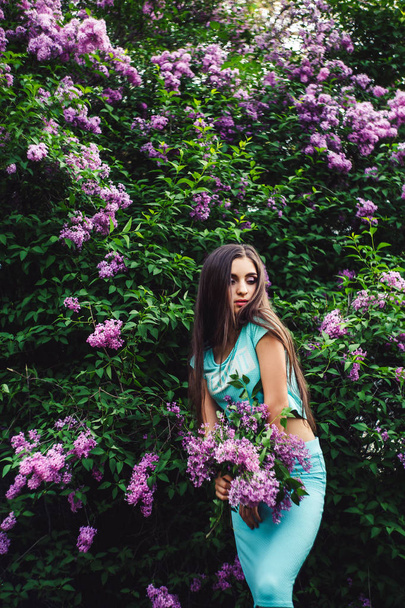 Maravillosa primavera. Linda chica joven disfruta de la naturaleza entre la flor de lila y sostiene un ramo
. - Foto, imagen
