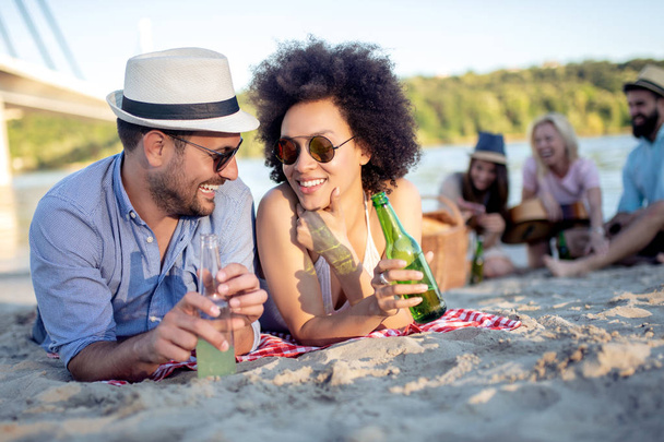 Jovem casal bonito se divertindo na praia, bebendo cerveja e sorrindo
. - Foto, Imagem