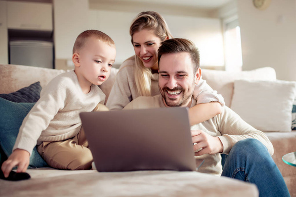 Šťastní rodiče s synem pomocí přenosného počítače v obývacím pokoji. - Fotografie, Obrázek