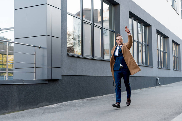 businessman in beige coat showing peace sign while running on street - Foto, imagen