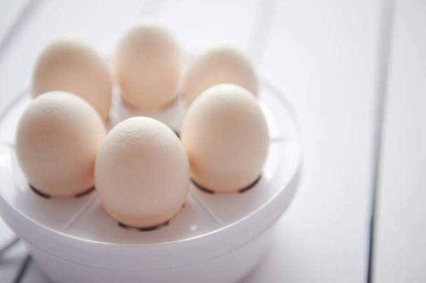 Chicken eggs in a egg electric cooker on a white wooden table - Photo, Image