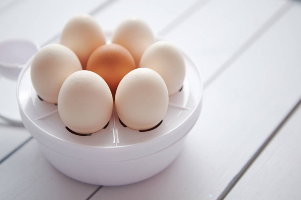 Chicken eggs in a egg electric cooker on a white wooden table - Photo, Image
