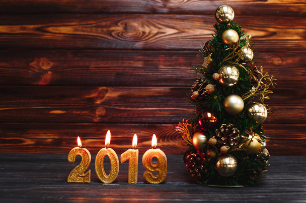 golden candles in form of numbers 2019 with christmas tree on wooden background - Фото, зображення