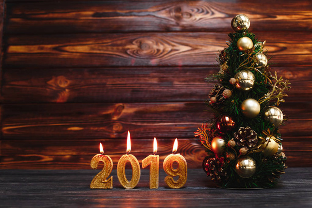 golden candles in form of numbers 2019 with christmas tree on wooden background - Fotó, kép
