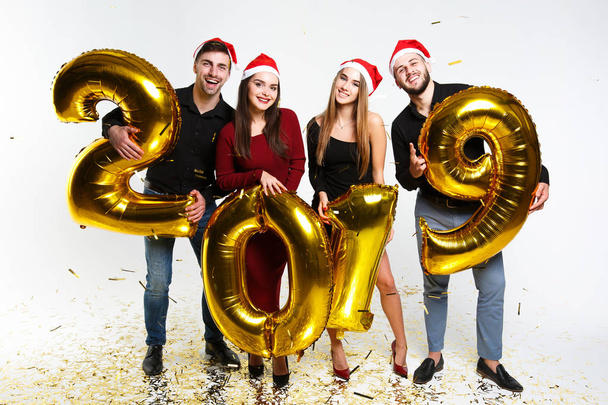 Retrato de grupo de amigos celebrando Año Nuevo, de pie con globos con números dorados en 2019 aislados sobre fondo blanco
 - Foto, Imagen