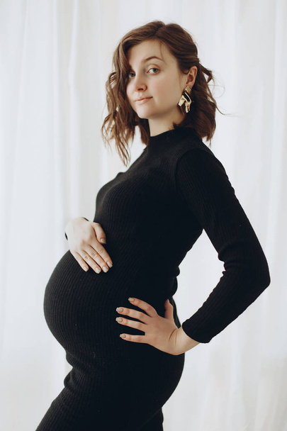 Happy young pregnant woman in stylish black dress holding belly  - Foto, Bild