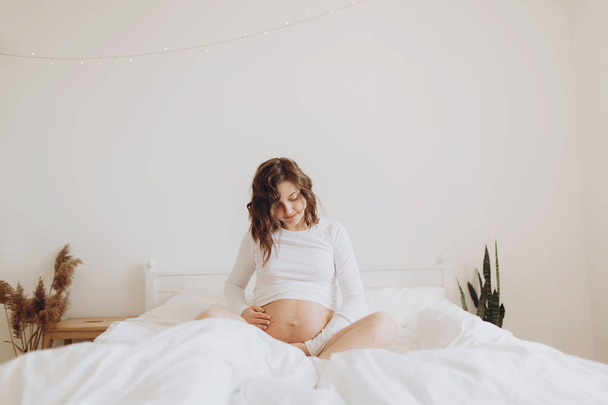Mujer embarazada feliz en blanco sosteniendo barriga golpe y relajarse en
 - Foto, imagen