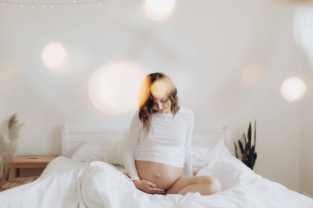 Счастливая беременная женщина в белом держит животик и расслабляется
 - Фото, изображение