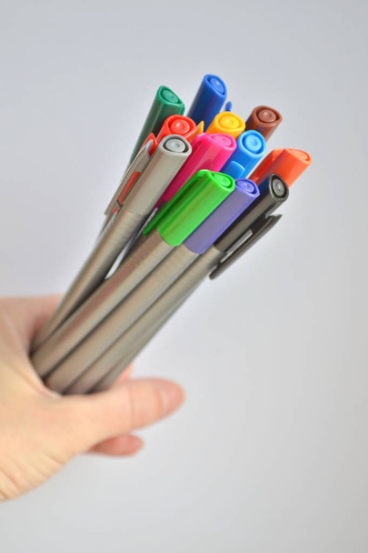 Ensemble de stylos multicolores tenant dans la main de la femme, sur fond blanc, orientés verticalement
 - Photo, image