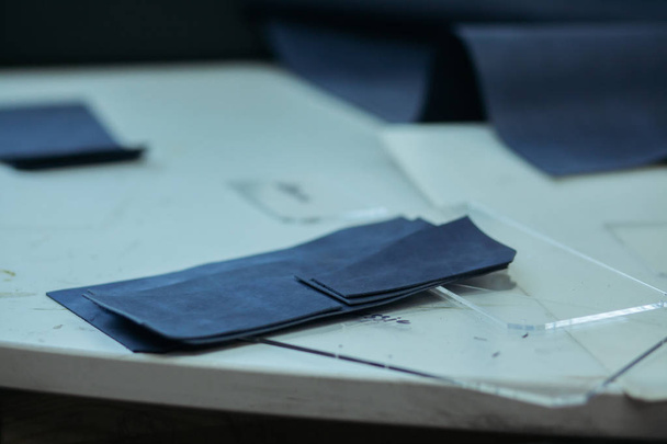 Making leather wallets on a sewing machine by a craftsman on a white table. Nearby are several ready-made leather wallets. On the table is a lamp and a sewing machine. - 写真・画像
