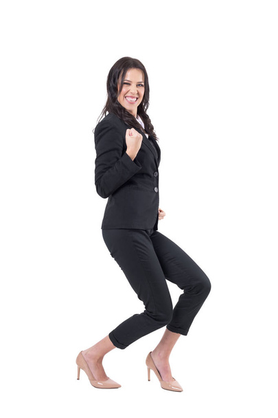 Ecstatic business woman in suit crouching with clenched fist celebrating success. Full body isolated on white background.  - Photo, Image