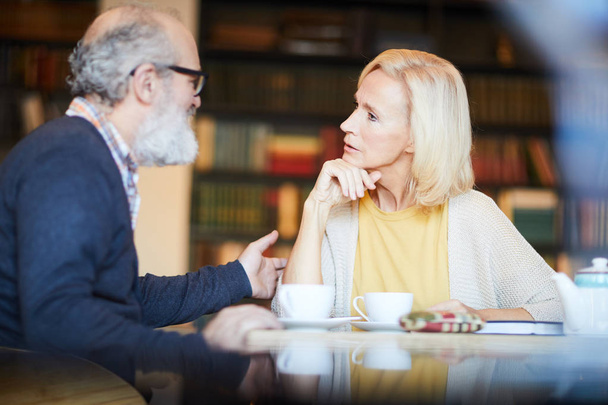 Blonde aged woman looking at bearded man during their conversation by cup of tea in cafe - Fotografie, Obrázek
