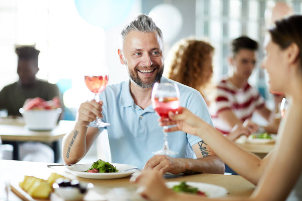 glücklicher Mann und seine Freundin stoßen mit Gläsern hausgemachter Getränke an, während sie am Tisch sitzen und Party genießen - Foto, Bild