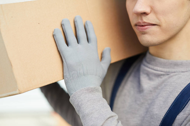 Close-up of content young mover in gloves carrying cardboard box on shoulder - Photo, Image