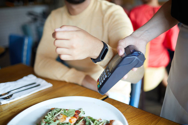 Homme contemporain tenant sa main avec smartwatch par la machine de paiement tout en payant pour le déjeuner
 - Photo, image
