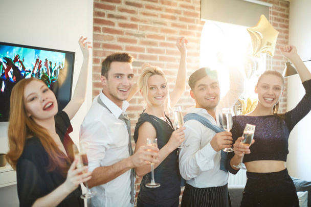 Ряд екстатичних молодих людей у розумному вбранні піднімають флейти шампанського, розважаючись на домашній вечірці
 - Фото, зображення