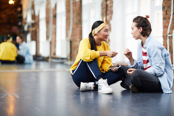 Молодой тренер консультирует ее ученицу во время перерыва между тренировками во время отдыха на полу в студии
 - Фото, изображение