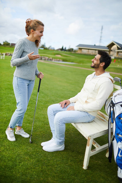 Joven hombre y mujer casual tener charla en el descanso entre entrenamientos de golf en el campo verde
 - Foto, Imagen
