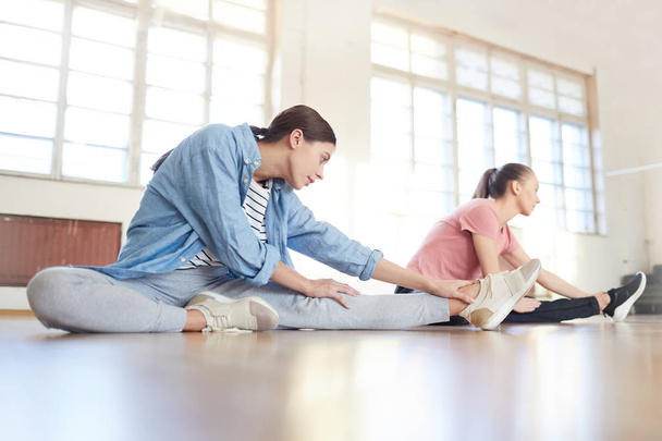 Молоді виконавці в активному одязі роблять вправи на підлозі під час занять в сучасній студії
 - Фото, зображення