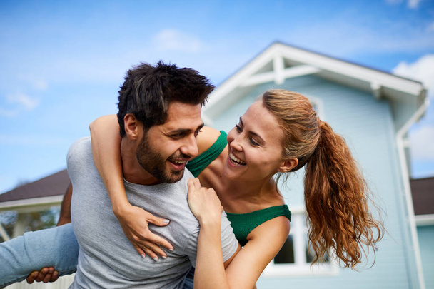 Веселая молодая женщина обнимает своего мужа, веселясь у своего нового дома
 - Фото, изображение