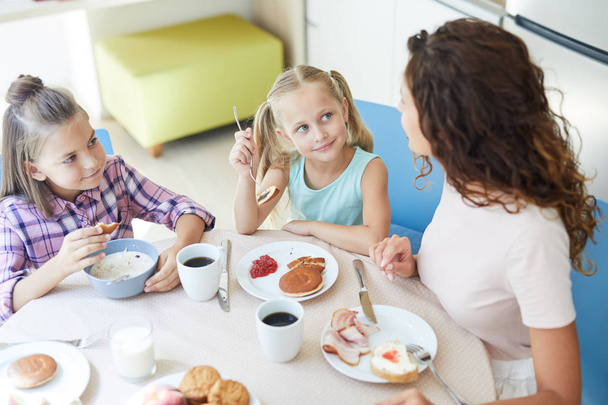 Little adorable girls looking at their mom by breakfast while eating tasty homemade food - Photo, Image