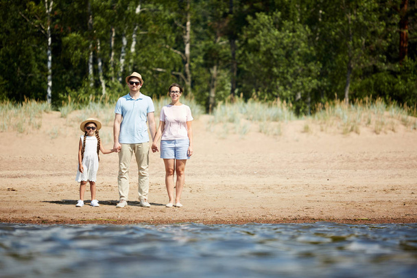 Teljes hosszúságú portréja boldog család kezében kéz állva a víz a strandon, és nézi a kamerát, másolás Space - Fotó, kép