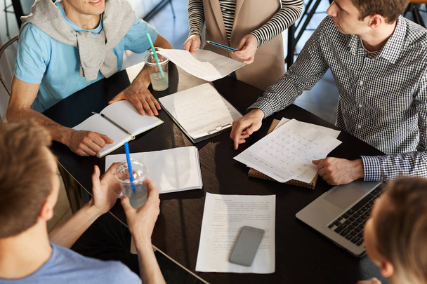 Высокоугловой кадр команды творческих бизнесменов, обсуждающих работу во время встречи, акцент на бумагах и документах на темном деревянном столе
 - Фото, изображение
