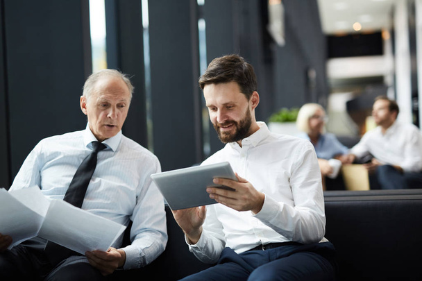 Dos hombres de negocios en ropa formal mirando a través de datos financieros en línea o estadísticas en la reunión
 - Foto, Imagen