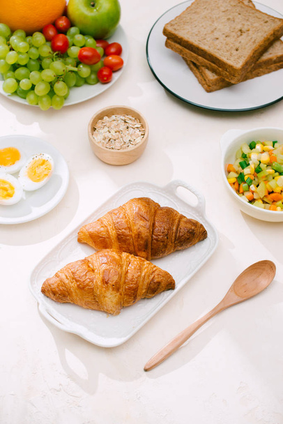 Café da manhã saudável servido com leite, croissants, ovo, cereais, aveia e frutas
. - Foto, Imagem