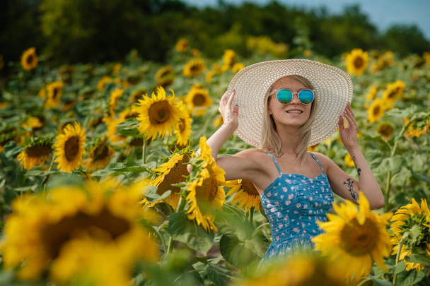 mooie zoete sexy meisje in een blauwe jurk lopen op een veld met zonnebloemen, glimlachend een mooie glimlach, vrolijke meisje, style, lifestyle, ideaal voor reclame en foto zon schijnt fel en sappig - Foto, afbeelding